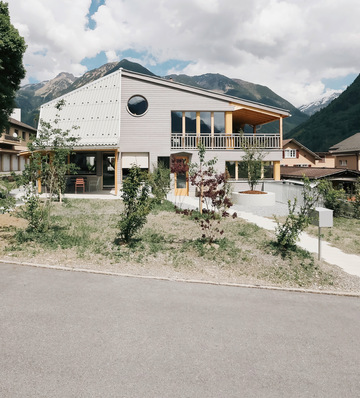 Modernes zweistöckiges Haus mit großen Fenstern, einem Balkon und Bergen im Hintergrund an einem teilweise bewölkten Tag. - © Foto: Reto Fuchs, Atelier Freienstein, Glarus